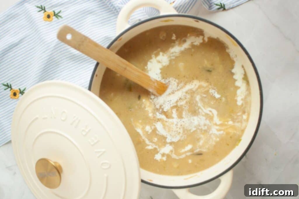 A cozy pot of rich, creamy soup, featuring a wooden spoon and a partially open lid, rests on a striped cloth adorned with intricate embroidered flowers, ready to be served.