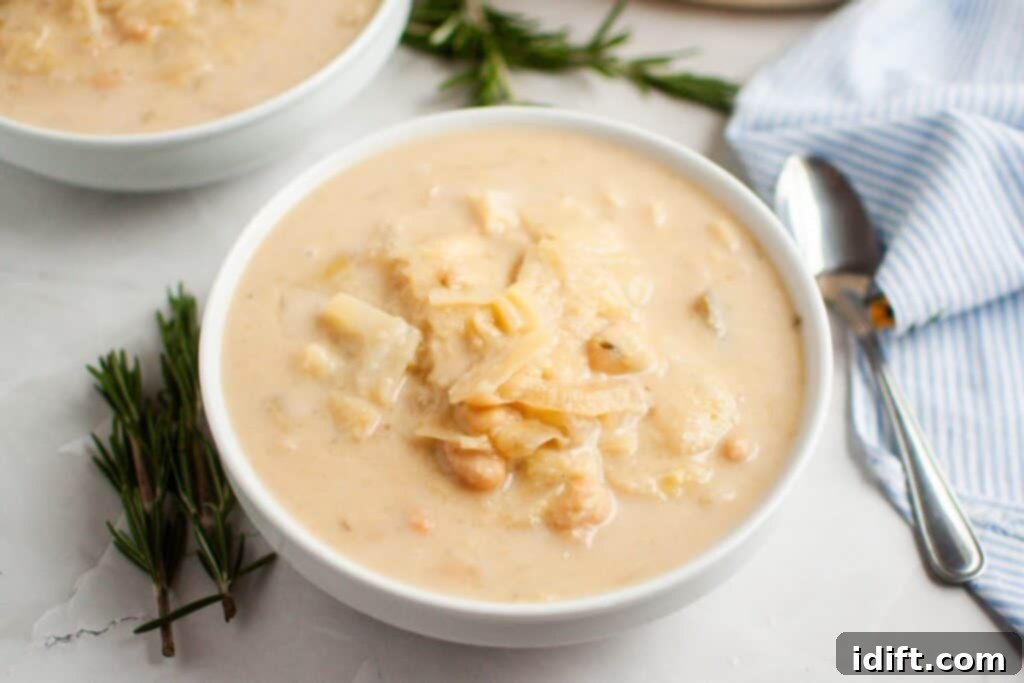 A cozy bowl of Cabbage and Bean Soup, garnished with aromatic sprigs of fresh rosemary, sits on a wooden surface next to a shining spoon and a crisp striped napkin, inviting warmth and flavor.