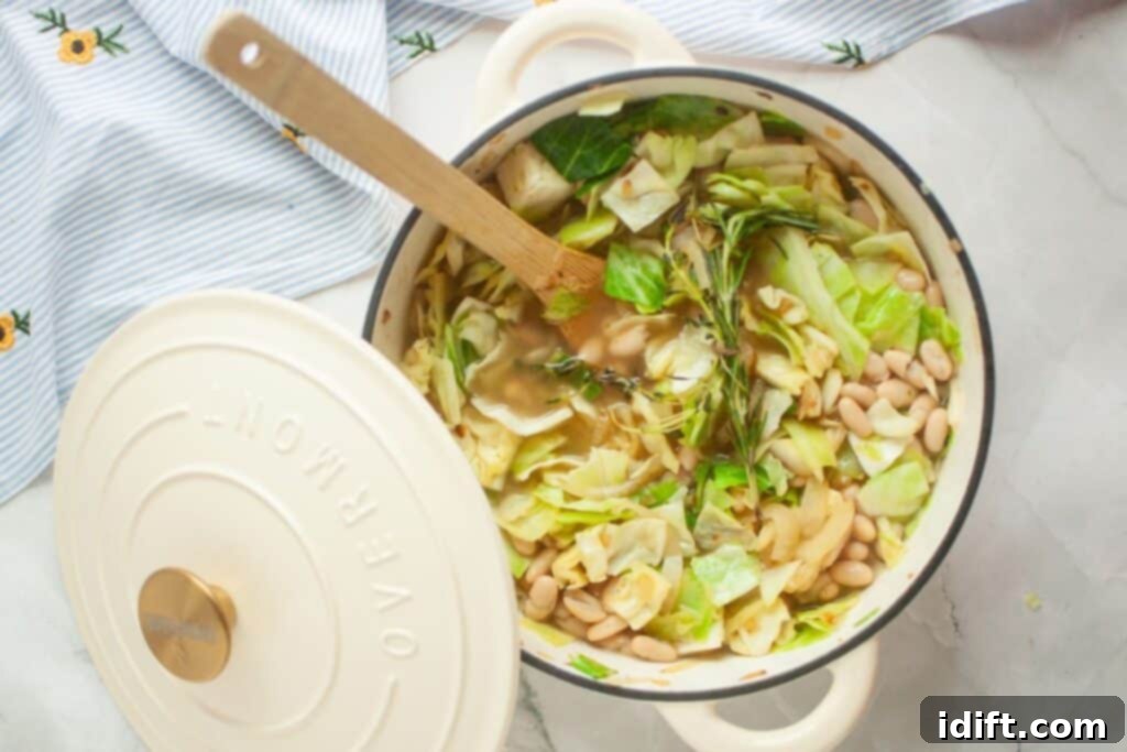 A vibrant pot of vegetable soup with cabbage, white beans, and fresh herbs. The lid is partially lifted, revealing the simmering goodness, while a wooden spoon rests invitingly inside, all set on a charming striped cloth with a daisy pattern.