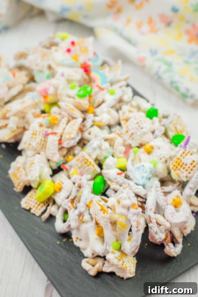 Emerald Enticement 2 Colorful snack mix with cereal pieces, pretzels, and candies coated in white frosting on a dark serving tray.