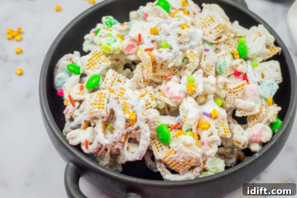 Emerald Enticement 10 A black bowl filled with a mix of cereal, pretzels, colorful candies, and marshmallows, coated in a white, sweet glaze.