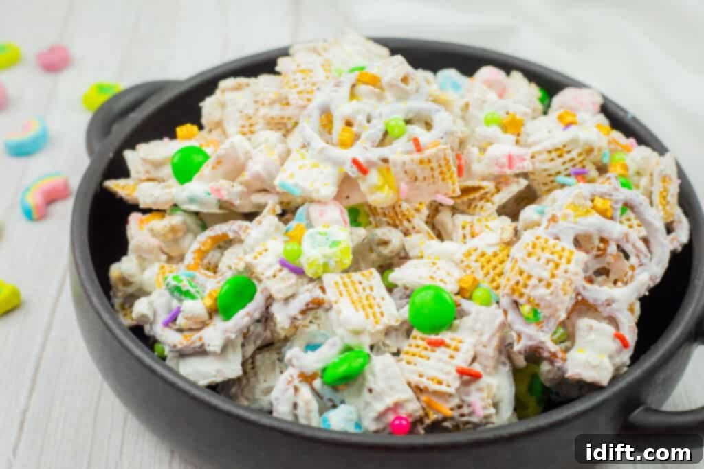 Emerald Enticement 3 A black bowl filled with a snack mix, including cereal squares, pretzels, colorful candy pieces, and coated in a white coating.