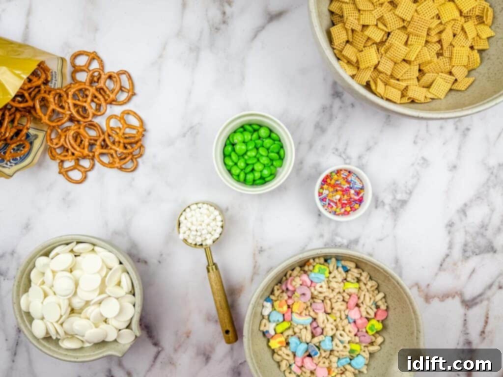 Emerald Enticement 5 Ingredients for a snack mix are arranged on a marble surface, including pretzels, cereal, chocolate wafers, green candy, mini marshmallows, sprinkles, and cereal with marshmallow bits.