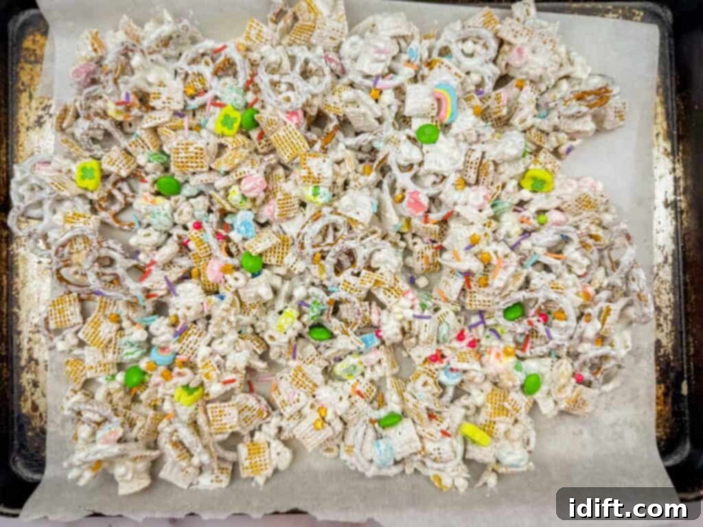Emerald Enticement 7 A tray of snack mix with pretzels, cereal, and colorful candies, coated in white confectionery on parchment paper.