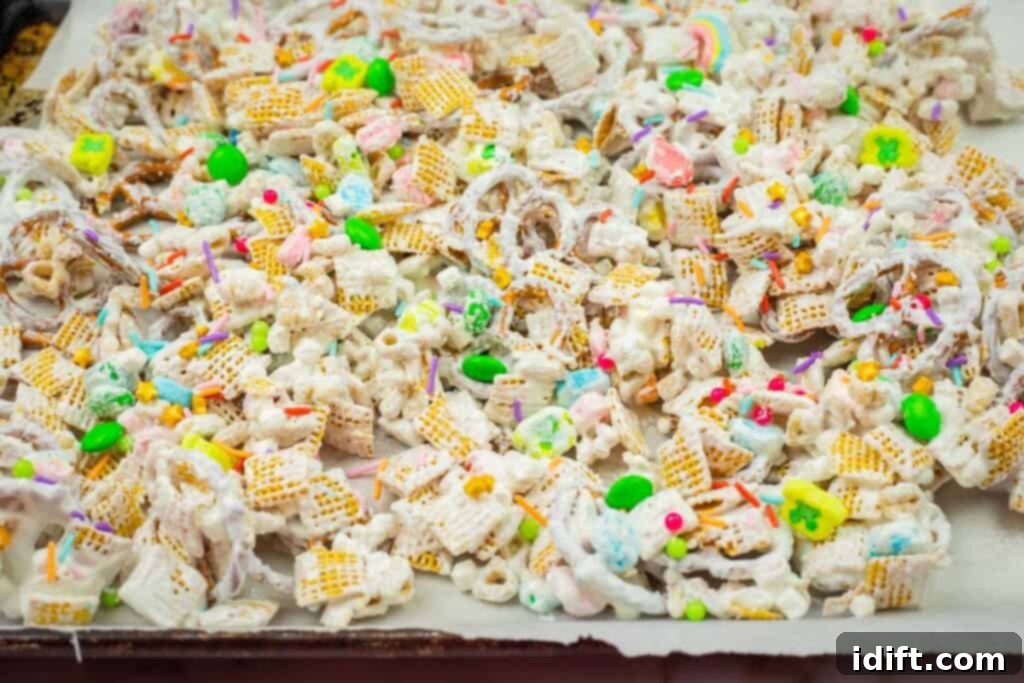 Emerald Enticement 8 A colorful snack mix with cereal, candy pieces, and pretzels covered in white chocolate and sprinkles on a lined baking sheet.