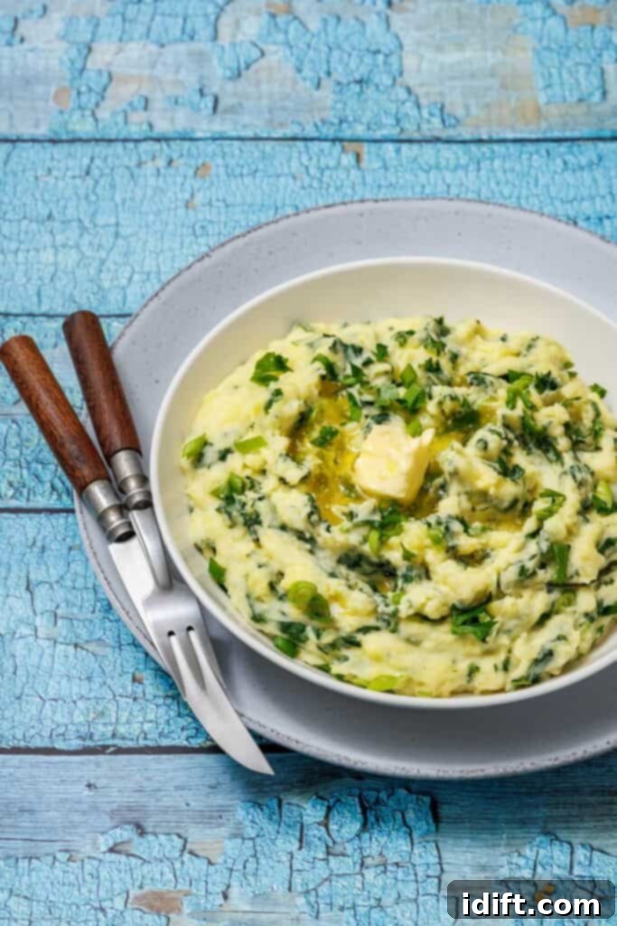 A bowl of Colcannon with Kale with parsley and melting butter on top, placed on a gray plate with a fork and knife on a rustic blue wooden table.