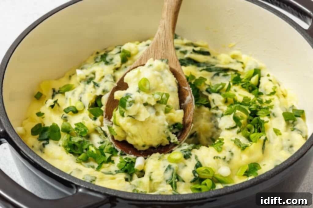 A pot of Colcannon with Kale mixed with chopped greens, garnished with sliced green onions, and a wooden spoon scooping some up.