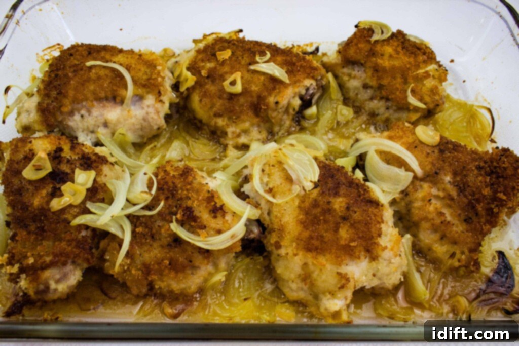 A close-up view of the perfectly oven baked chicken thighs, showing the crispy skin and tender meat, adorned with fragrant garlic and onion pieces.