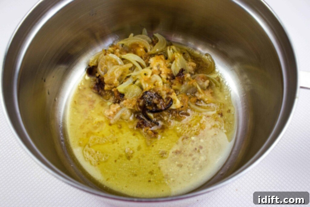 Using a spatula to carefully scrape all the flavorful drippings, onions, and garlic chunks from the baking dish into a pot, forming the base for the rich gravy.