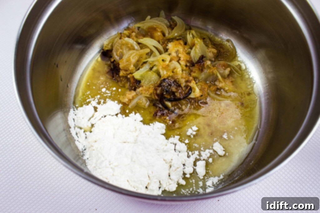 All-purpose flour being added to the rich pan drippings and aromatic chunks in a pot, creating a flavorful paste as the first step for the creamy gravy.