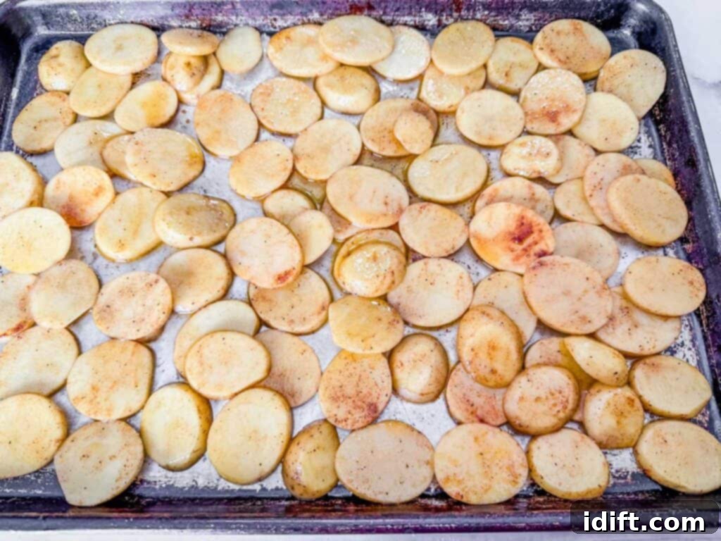 Slices of potatoes spread evenly on a baking tray, seasoned and baked until golden brown.