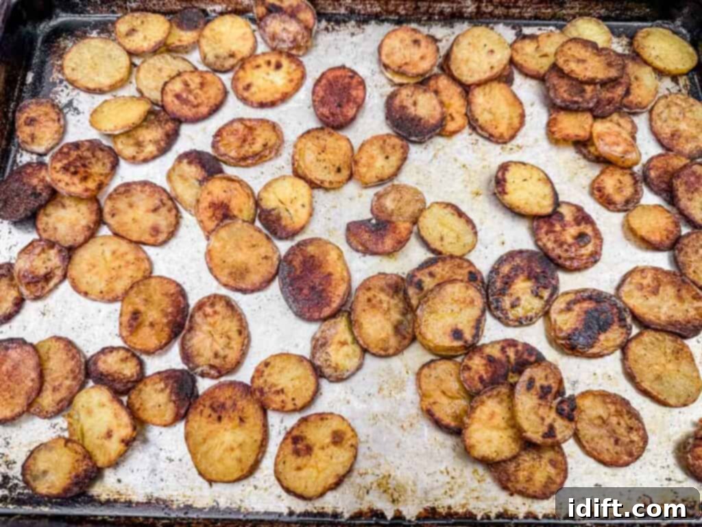 Sliced roasted potatoes on a baking sheet, some pieces are browned and crispy.