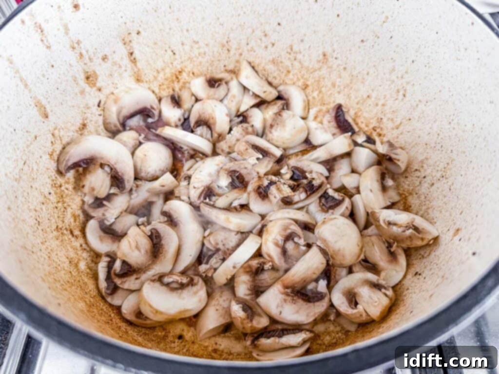 Hearty Beef Stroganoff Soup 7 Thinly sliced mushrooms are expertly sautéed in a large pot on the stovetop, developing a rich, deep brown color as they cook.