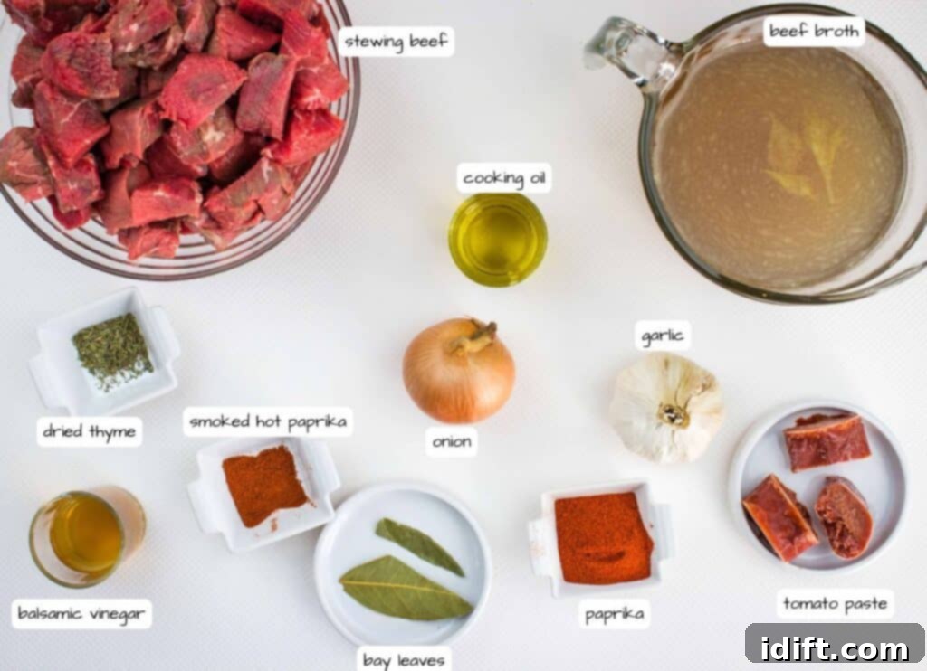 Hearty Hungarian Goulash 4 An array of fresh, high-quality ingredients for authentic Hungarian Goulash, including cubed stewing beef, whole onions, fresh garlic cloves, a bottle of balsamic vinegar, a carton of beef broth, a tube of tomato paste, cooking oil, and bowls of paprika, smoked paprika, dried thyme, and bay leaves, all neatly arranged on a wooden surface.