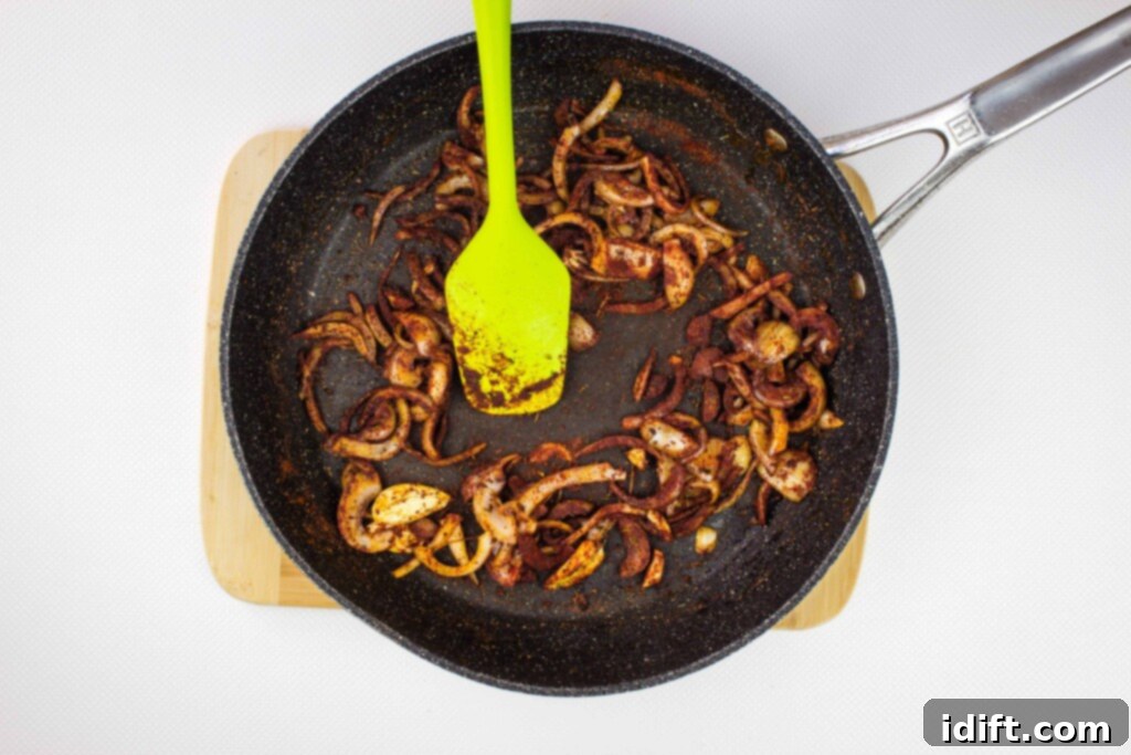 Hearty Hungarian Goulash 7 Vibrant red paprika and other spices being stirred into sautéed onions and garlic in a skillet, creating a fragrant base for the goulash.
