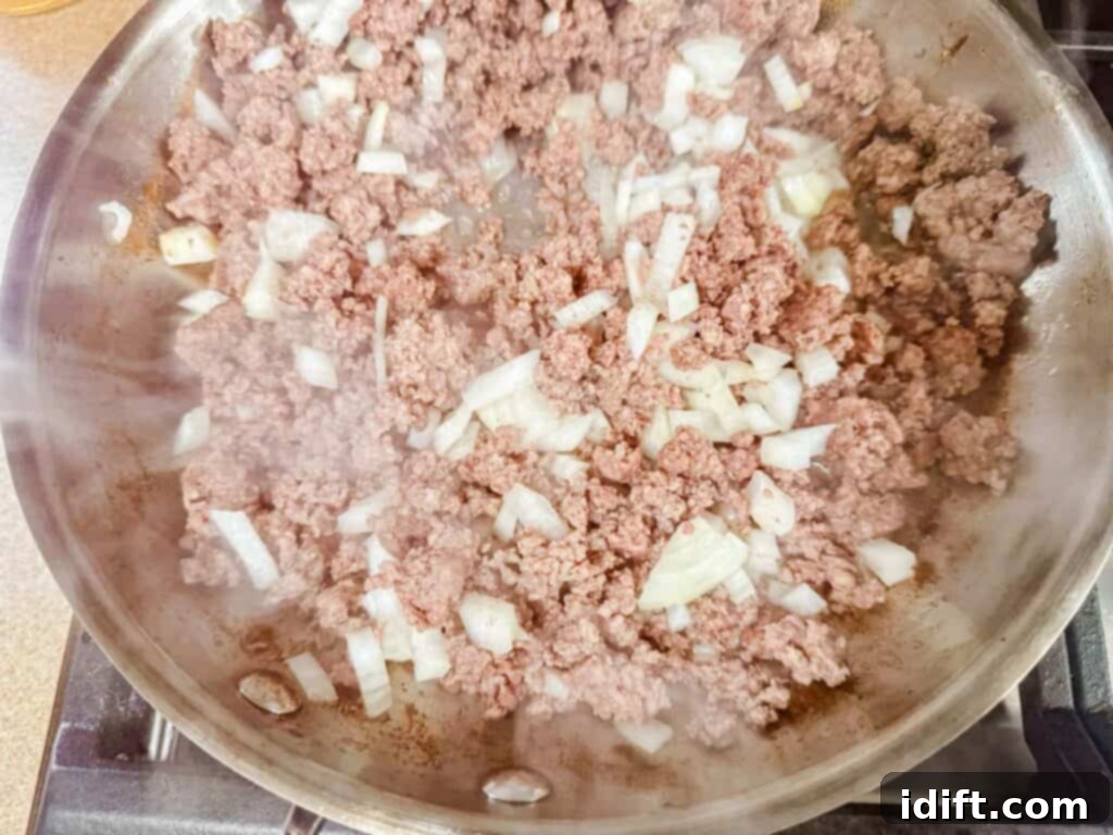 Ground beef and chopped onions cooking in a skillet, with steam rising.