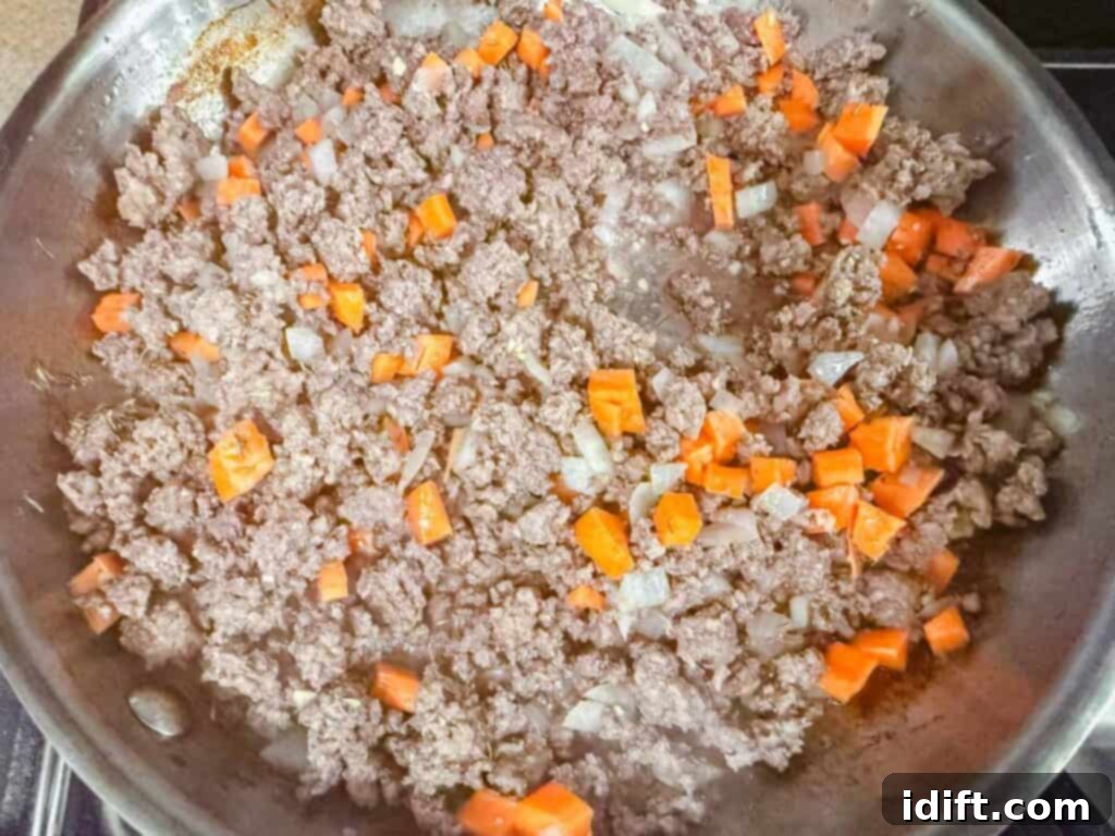 Chopped carrots and onions cooking with ground beef in a frying pan.