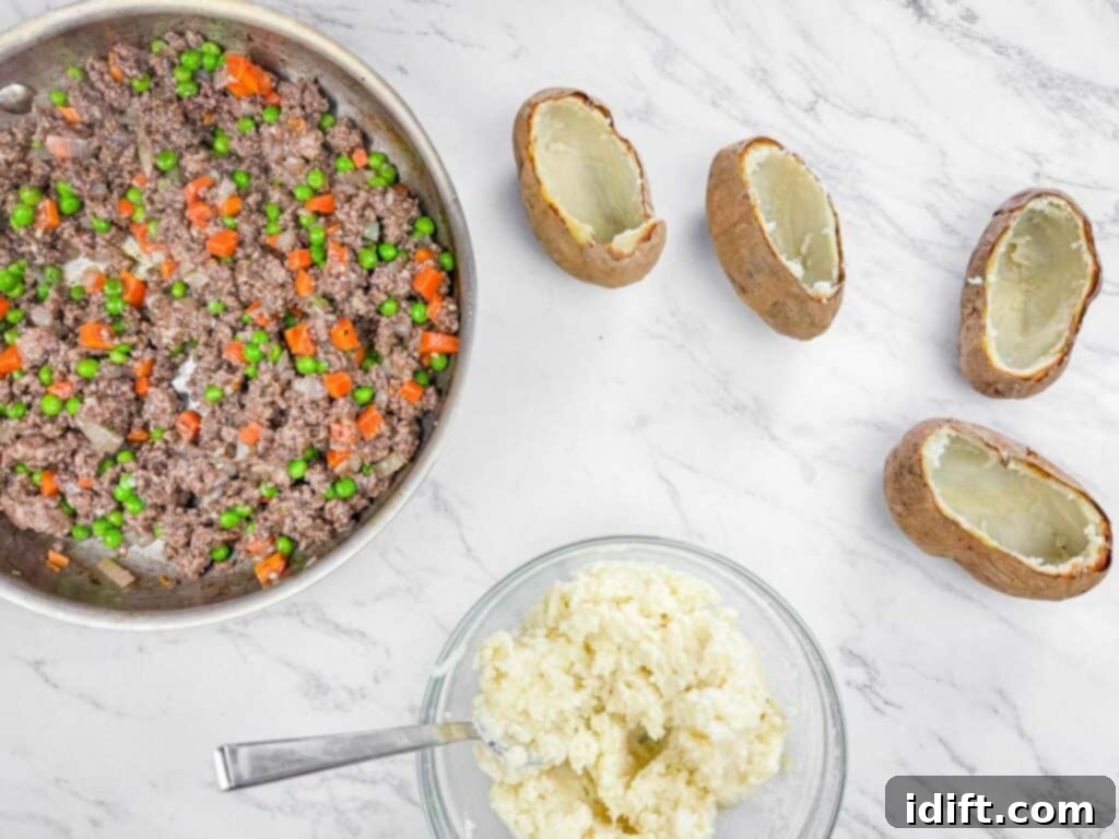 Skillet with ground beef, carrots, and peas; a bowl of mashed potatoes with a spoon; four hollowed potato skins on a marble surface.