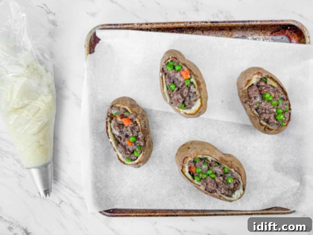 Four baked potatoes filled with ground beef, peas, and carrots on a parchment-lined tray. A piping bag with a star nozzle is nearby.