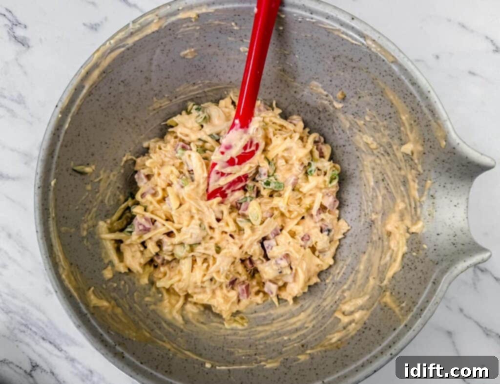 Golden Baked Reuben Dip 5 Bowl of mixed ingredients with a red spatula on a marble surface.