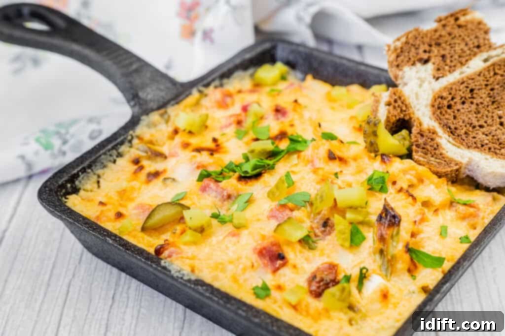 Golden Baked Reuben Dip 7 Hot Reuben Dip with chopped dill pickles and herbs in a square skillet served on a slate board with sliced brown bread.