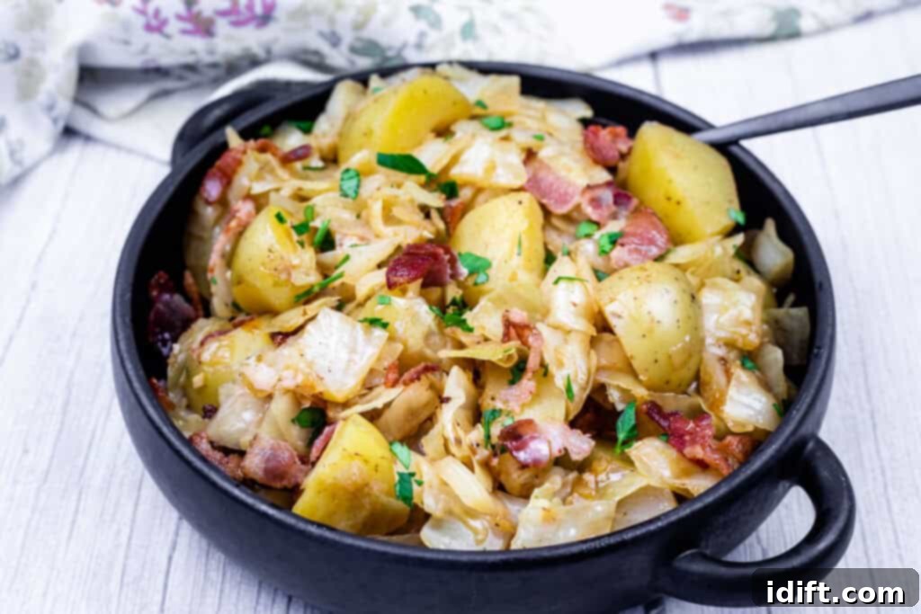 A black bowl filled with Cabbage & Potatoes with Bacon with a spoon on the side.