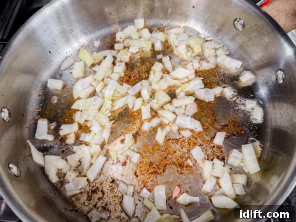 Chopped onions cooking in a stainless steel pan with browned bits on the surface.