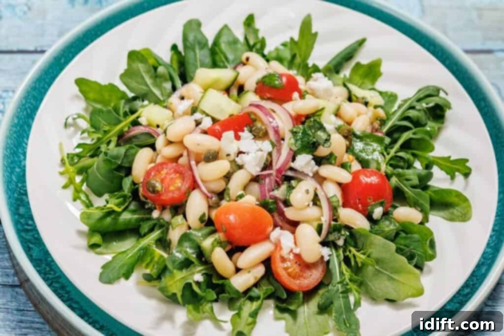 A plate of White Bean Salad with arugula, white beans, cherry tomatoes, red onion, cucumber, and crumbled cheese.