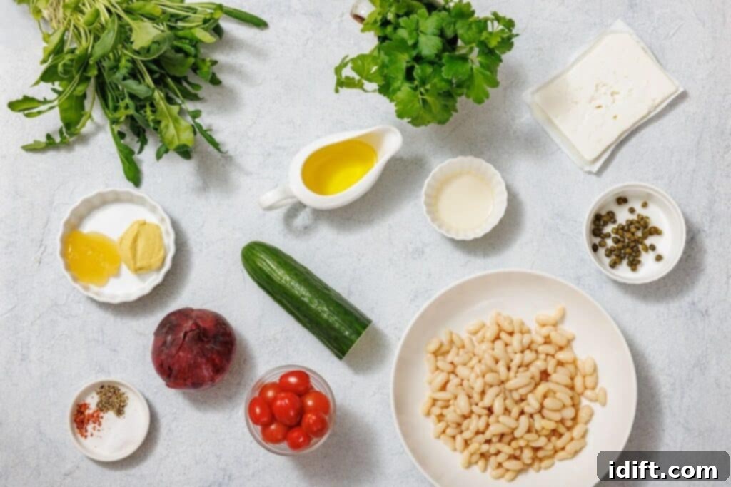 Ingredients for White Bean Salad arranged on a light surface: herbs, feta, olive oil, mustard, cream, capers, white beans, cucumber, cherry tomatoes, a beetroot, and spices.