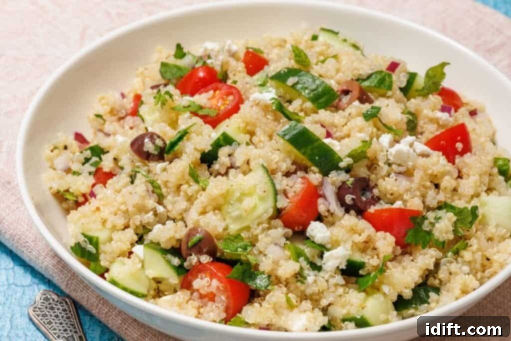 A large, inviting bowl of Mediterranean Quinoa Salad, richly composed of fluffy quinoa, bright red cherry tomatoes, fresh green cucumber slices, dark Kalamata olives, thinly sliced red onion, crumbled white feta cheese, and a generous sprinkle of fresh parsley. The salad is beautifully presented on a light blue tablecloth, highlighting its colorful and appealing freshness.