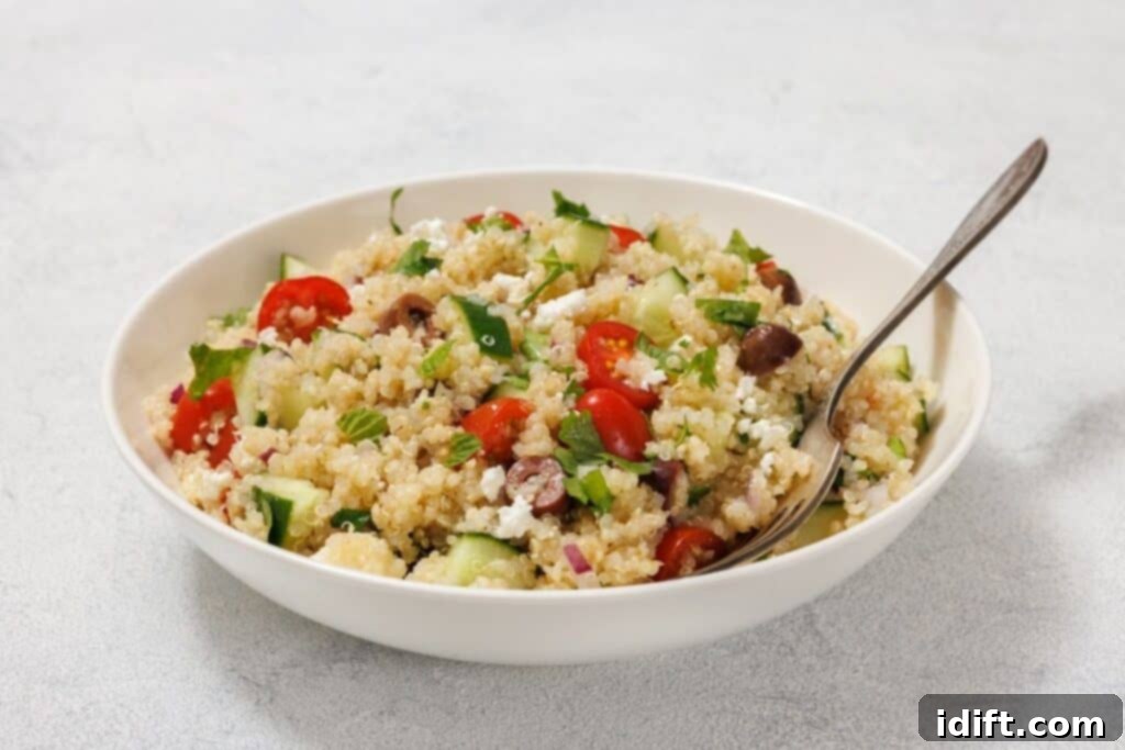 A beautifully presented bowl of Mediterranean Quinoa Salad, filled with a vibrant mix of quinoa, cherry tomatoes, cucumbers, olives, feta cheese, and fresh herbs. A serving spoon is gently placed in the bowl, which sits on a clean, light surface, inviting enjoyment.