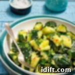 A bowl of cucumber salad with sesame seeds and herbs, accompanied by a fork. There's a small dish of salt and a ceramic jug in the background on a blue wooden table.