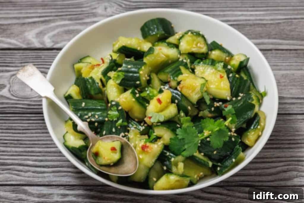 A delectable Smashed Cucumber Salad garnished with an abundance of toasted sesame seeds, fresh cilantro leaves, and a sprinkle of vibrant red pepper flakes, served gracefully with a metal spoon on a smooth wooden surface.
