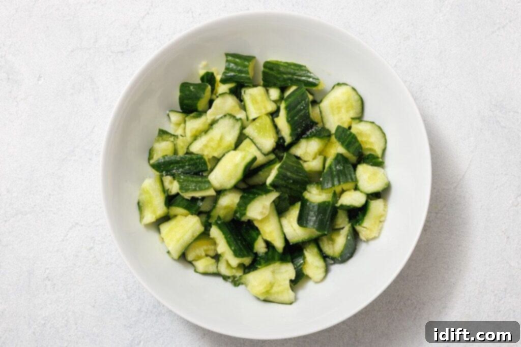 A pristine white bowl brimming with expertly smashed and torn cucumber pieces, glistening slightly, ready for salting to draw out excess moisture.