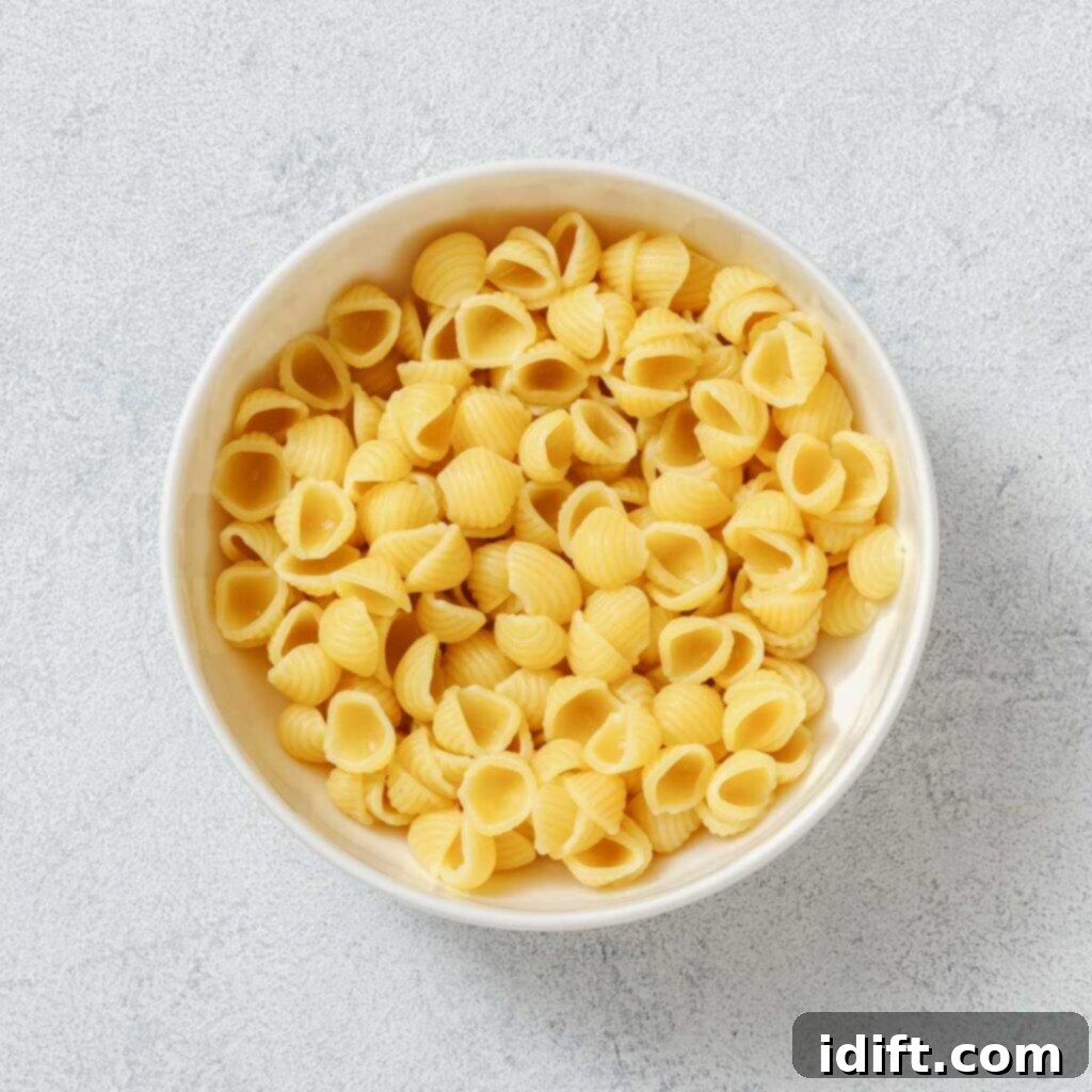 Vibrant Spring Minestrone 7 A white bowl filled with uncooked shell-shaped pasta on a light textured surface.