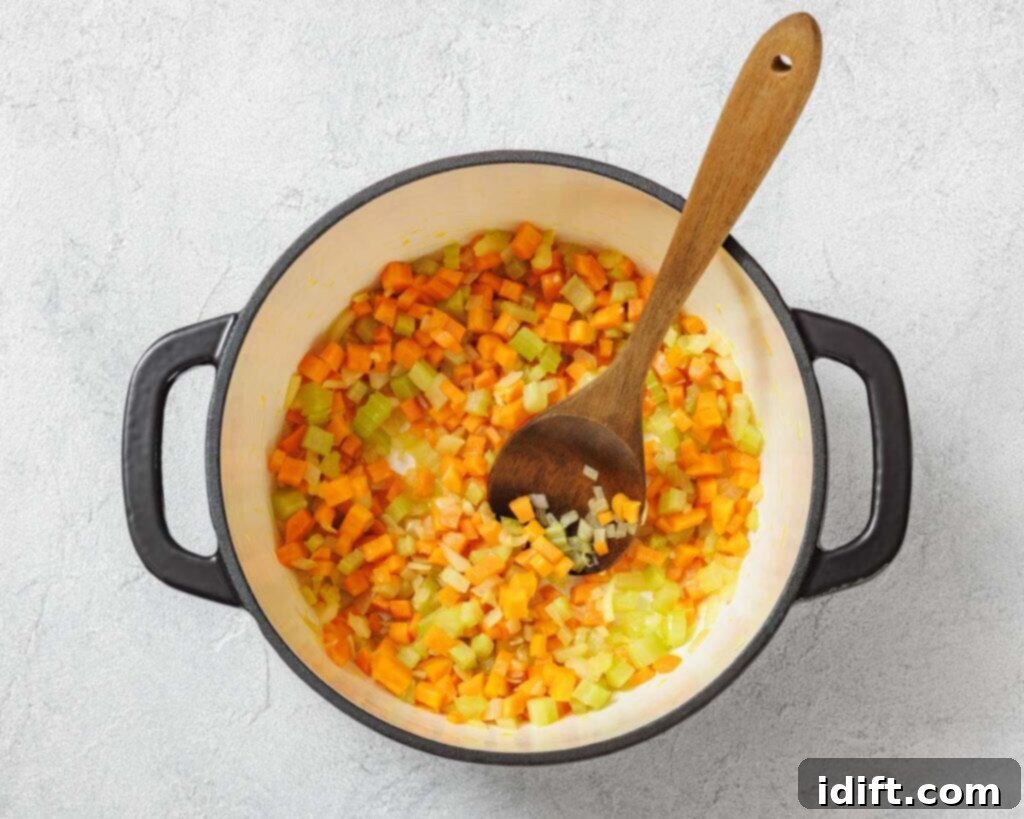 Vibrant Spring Minestrone 8 Diced carrots, celery, and onions are being sautéed in a large pot with a wooden spoon on a light surface.