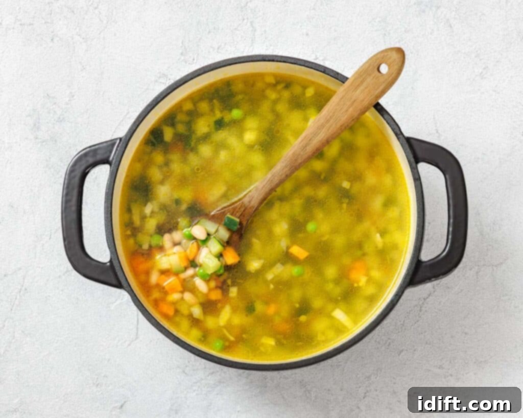 Vibrant Spring Minestrone 9 Pot of vegetable soup with a wooden spoon, containing peas, carrots, corn, and green onions, on a textured white surface.