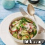 Bowl of Radish Salad with herbs on a white plate. Vintage fork and spoon on the side. Light blue wooden table background with a small jug and a napkin.