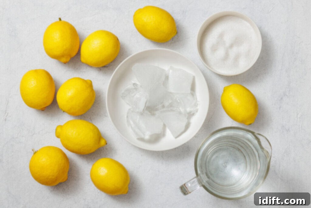 Perfectly Simple Lemonade 5 Flat lay of fresh lemons, a bowl of sugar, ice cubes on a plate, and a glass pitcher of water, arranged on a light-colored surface, showcasing the ingredients for homemade lemonade.