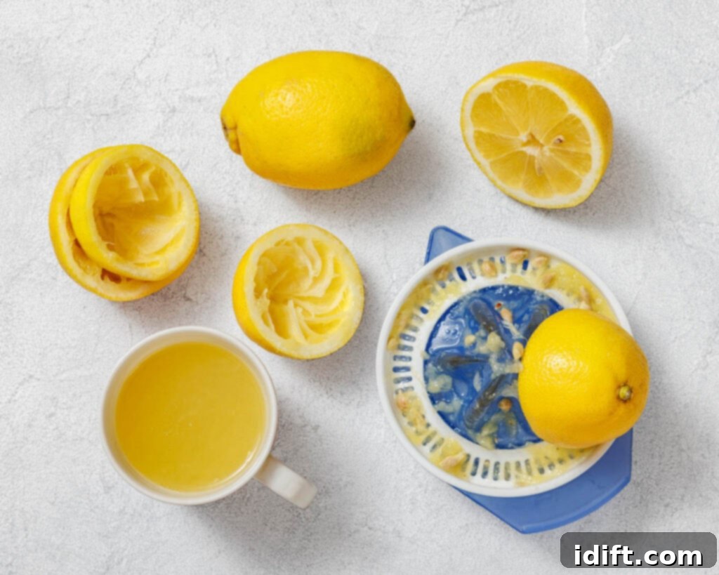 Perfectly Simple Lemonade 7 Flat lay of freshly squeezed lemons, a manual citrus juicer with pulp and seeds, and a cup filled with lemon juice on a textured light-colored surface.