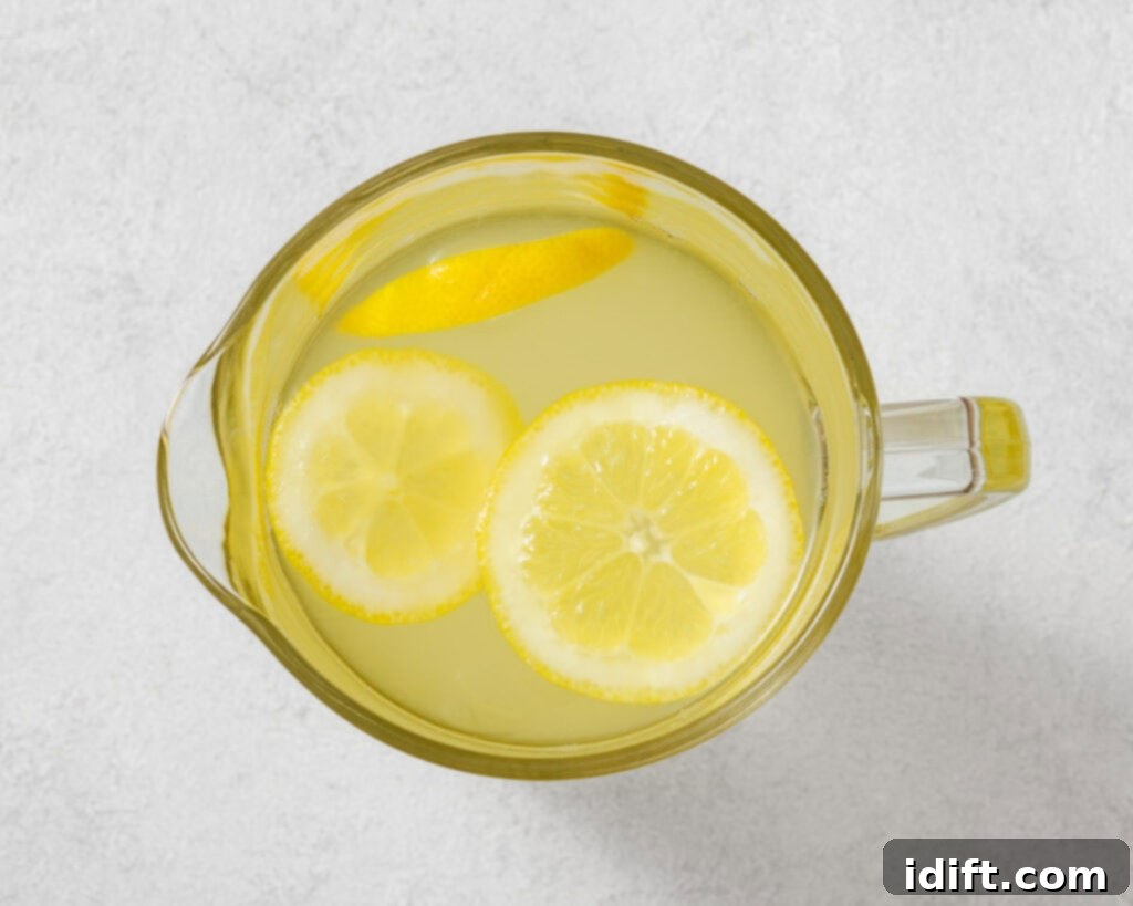 Perfectly Simple Lemonade 8 Top-down view of a clear pitcher with lemonade and lemon slices on a light gray surface.