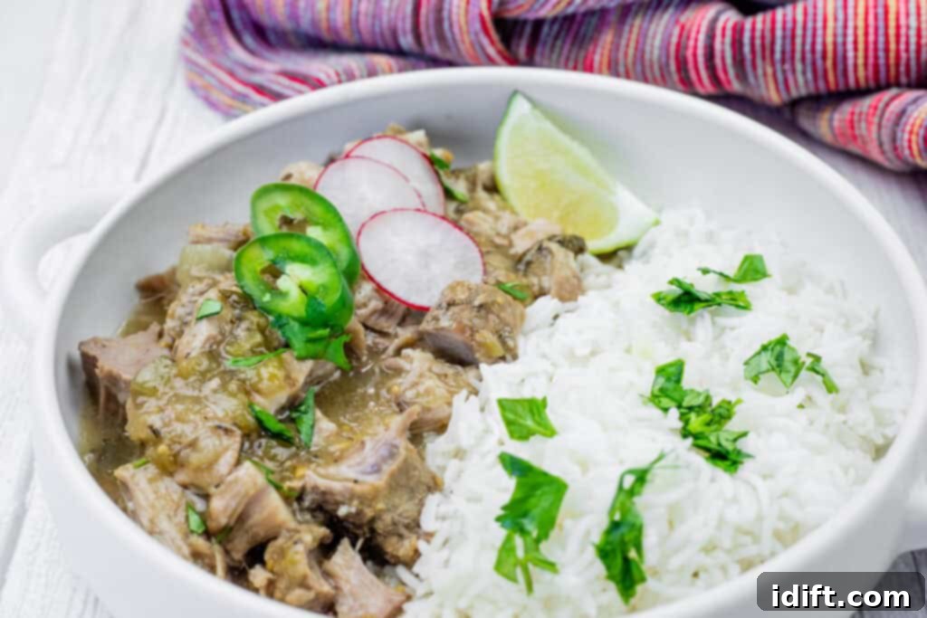 Tender Slow Cooker Pork Chile Verde 9 A white bowl filled with chile verde pork stew and white rice, garnished with sliced radishes, jalapenos, lime, and cilantro. A colorful cloth is in the background.