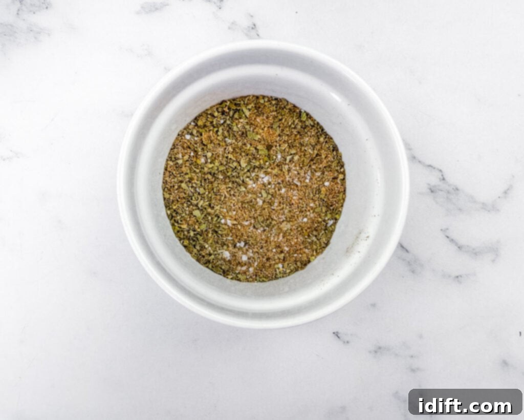 Tender Slow Cooker Pork Chile Verde 6 Overhead shot of a white bowl containing a mixture of dried herbs and spices, resting on a white marble surface with gray veins.