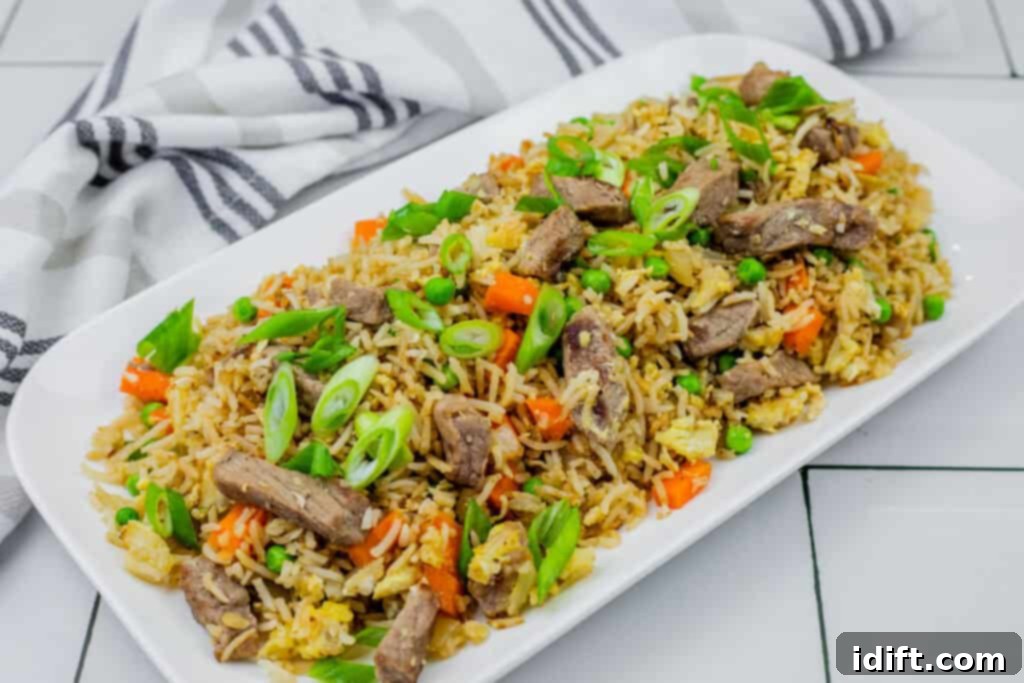 Steakhouse Fried Rice 11 steak fried rice in a white platter on white tiles with striped cloth on the side.