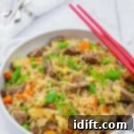 Steakhouse Fried Rice 12 Steak fried rice in a white bowl with handles, red chopsticks on top and folded white napkin on background.