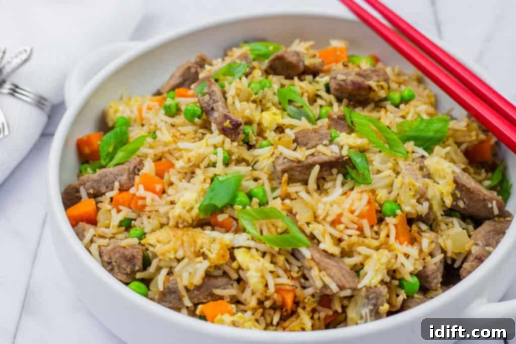 Steakhouse Fried Rice 3 steak fried rice in a white bowl with handles and red chopsticks on top.