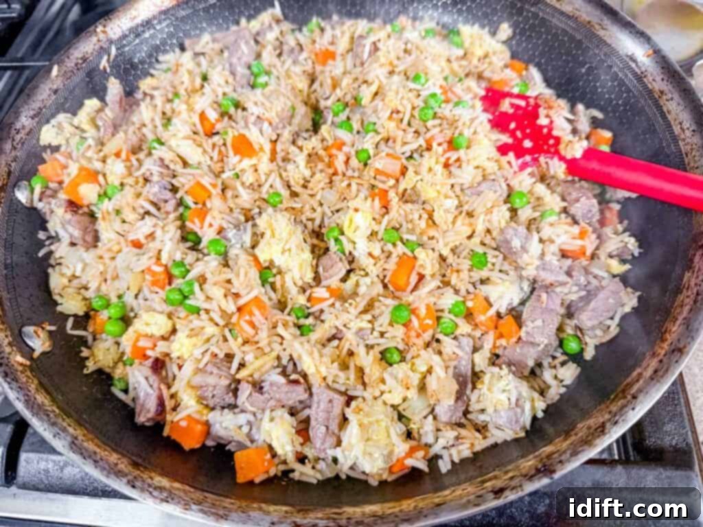 Steakhouse Fried Rice 9 cooked steak fried rice in a pan with red spatula.