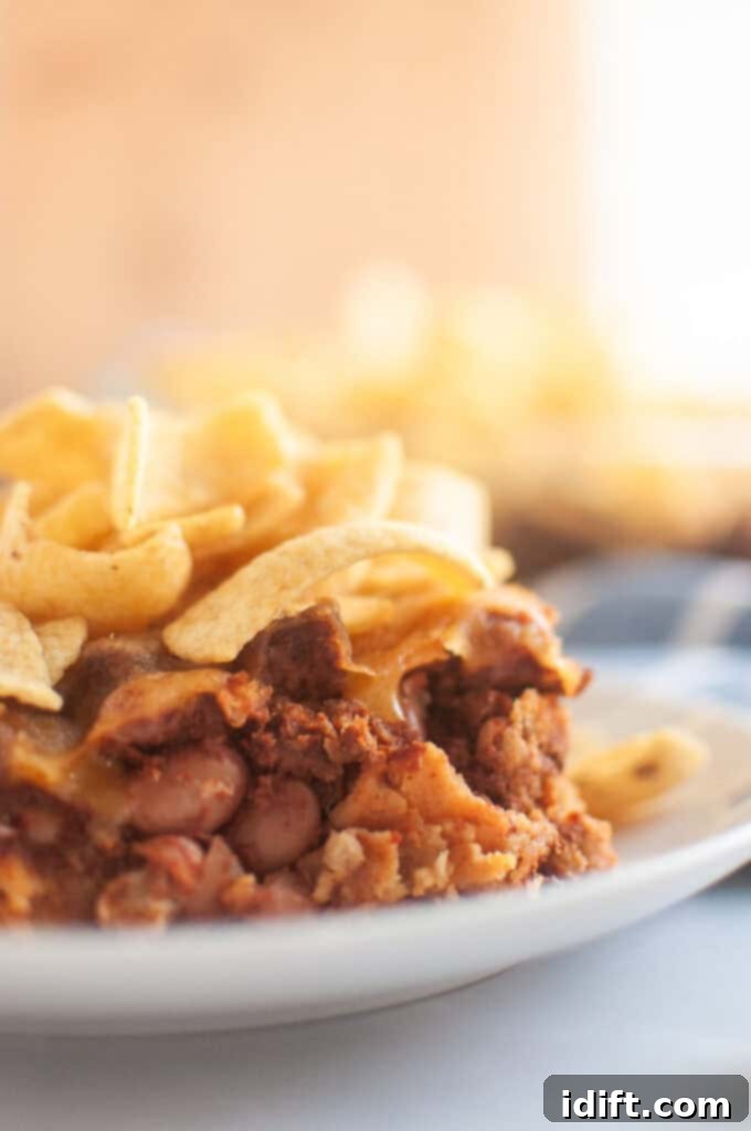 A close up take of Frito Pie in a small white plate on a white table with corn chips on top.
