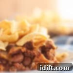 A close up take of Frito Pie in a small white plate on a white table with corn chips on top.