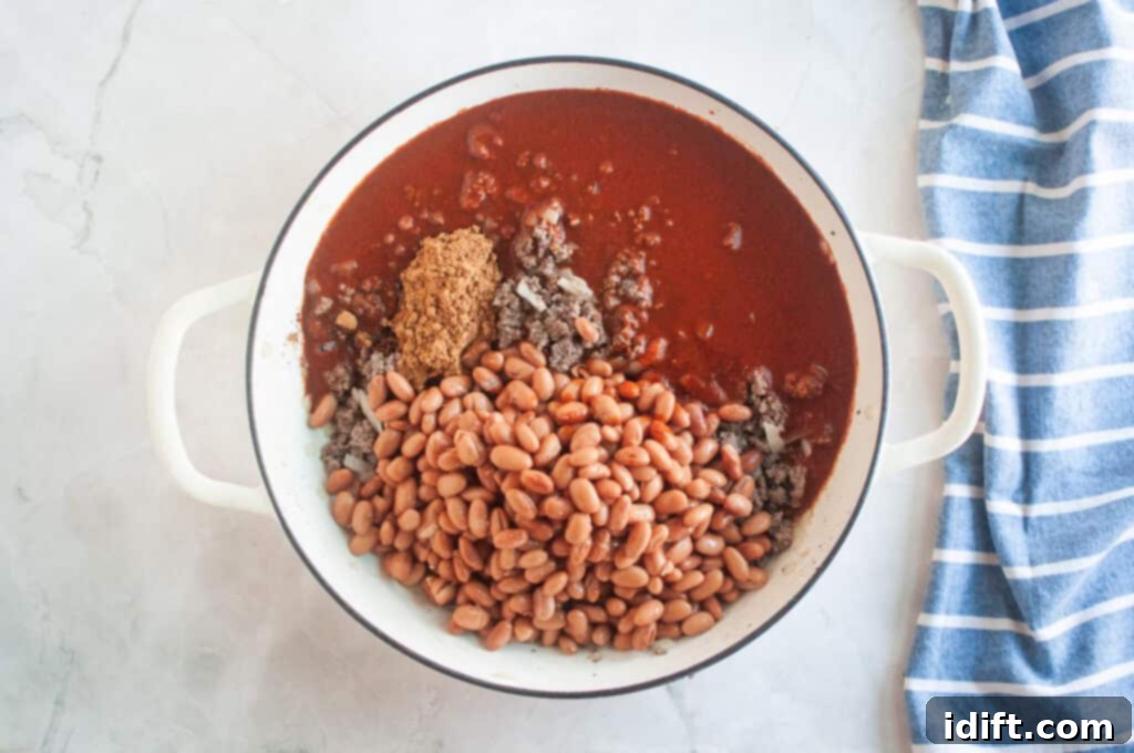 Overhead shot of cooked ground beef, onions, spices, chili sauce, and beans in a white pot.